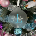 Decorative ornament with 'Lachlan' and a blue 'L' hanging on a Christmas tree.