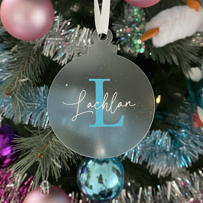 Decorative ornament with 'Lachlan' and a blue 'L' hanging on a Christmas tree.