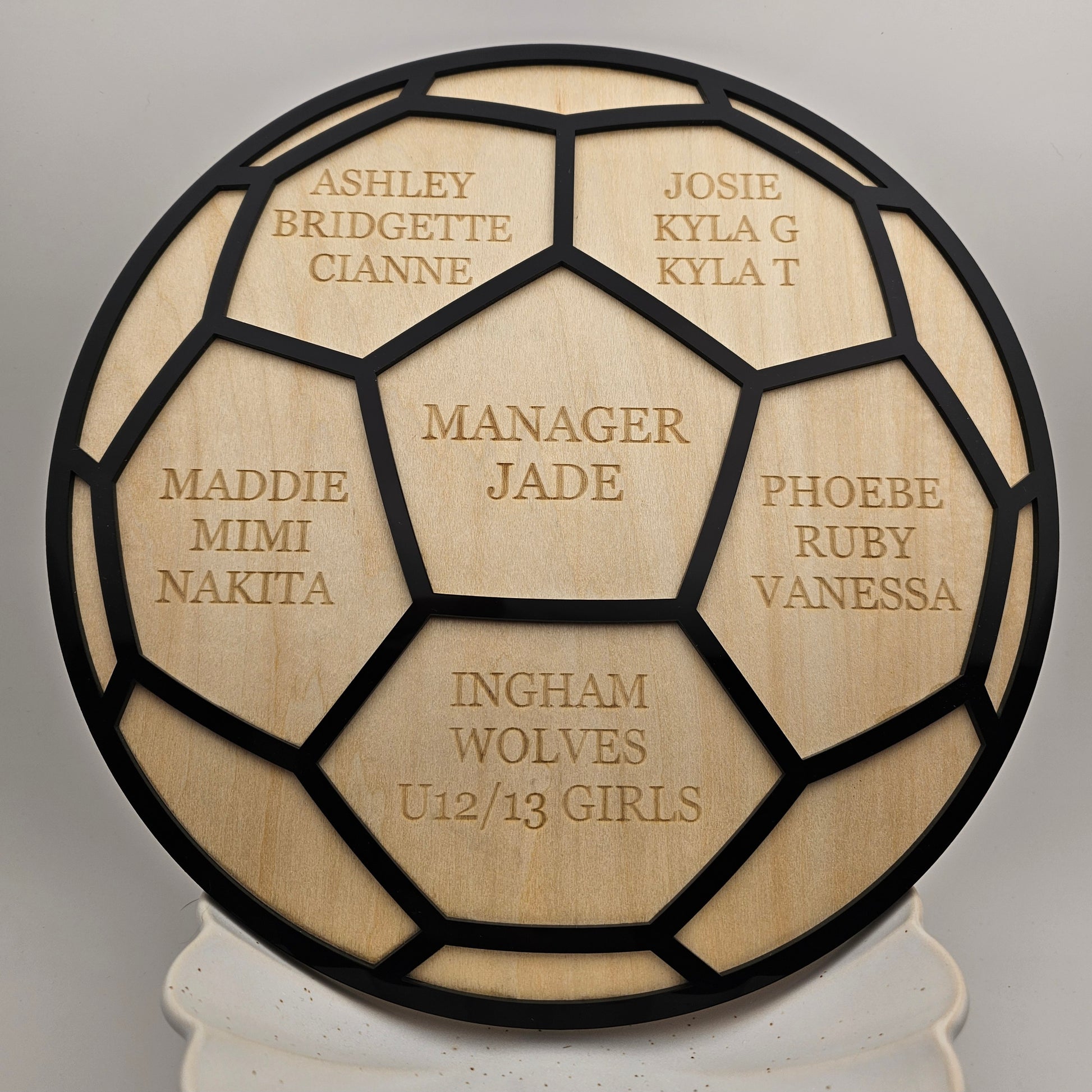 Wooden plaque with engraved names and text, resembling a soccer ball design.