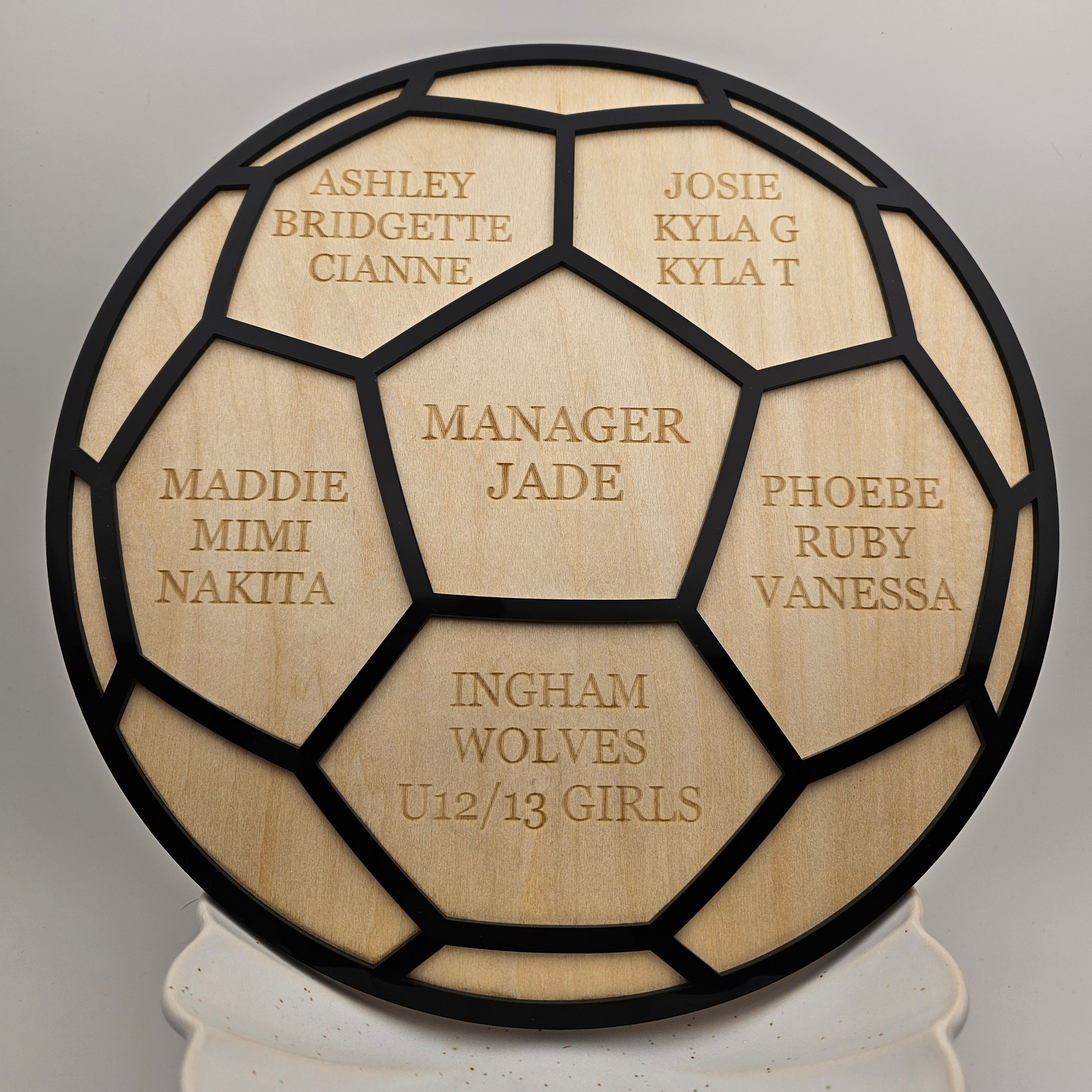 Wooden plaque with engraved names and text, resembling a soccer ball design.