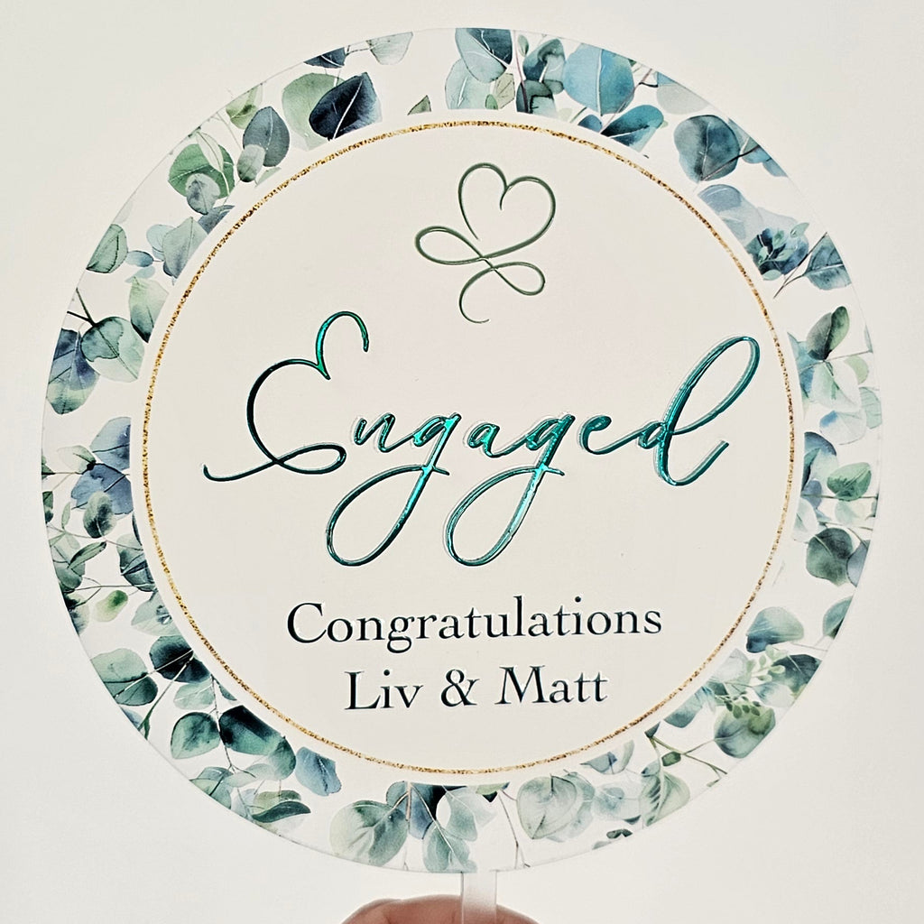 Round card with floral design and 'Engaged' text held by a hand on a white surface