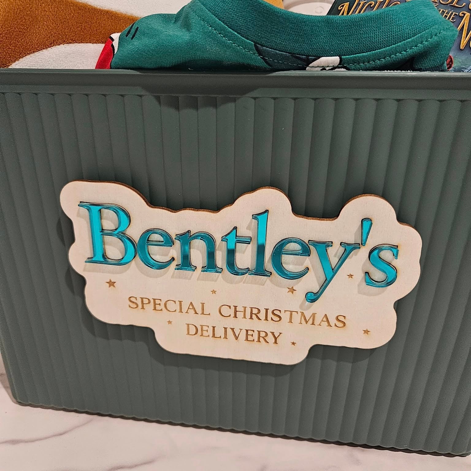 Gray storage bin with 'Bentley's Special Christmas Delivery' label, surrounded by festive items.