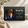 Memorial plaque for a dog named Bundy Boy with a photo of the dog wrapped in a colorful blanket, placed on a surface with a candle and plant in the background.
