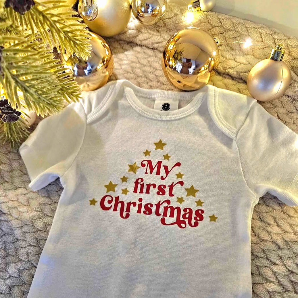 Baby onesie with 'My first Christmas' text on a textured surface with Christmas decorations.