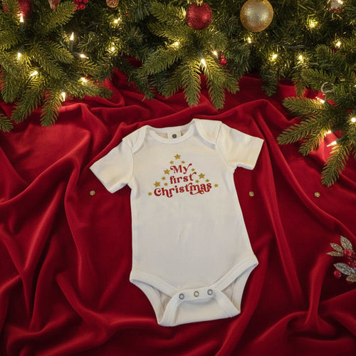 Baby onesie with 'My first Christmas' text on a textured surface with Christmas decorations.