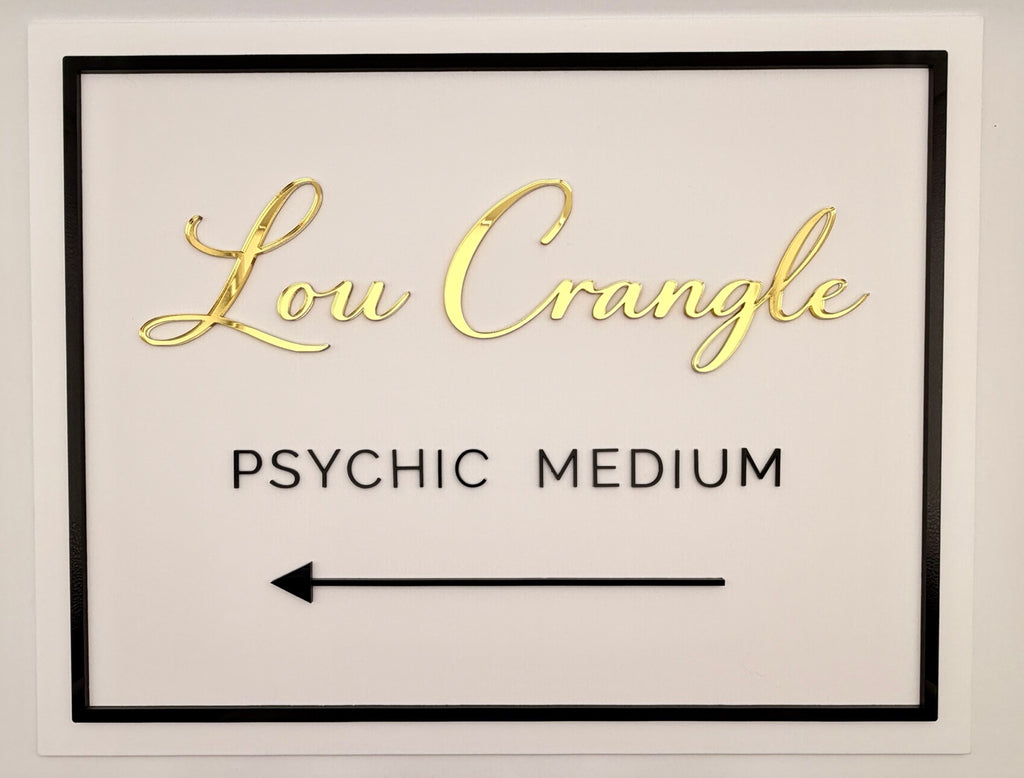 Framed sign with 'Lou Crangle Psychic Medium' text in gold on a white background
