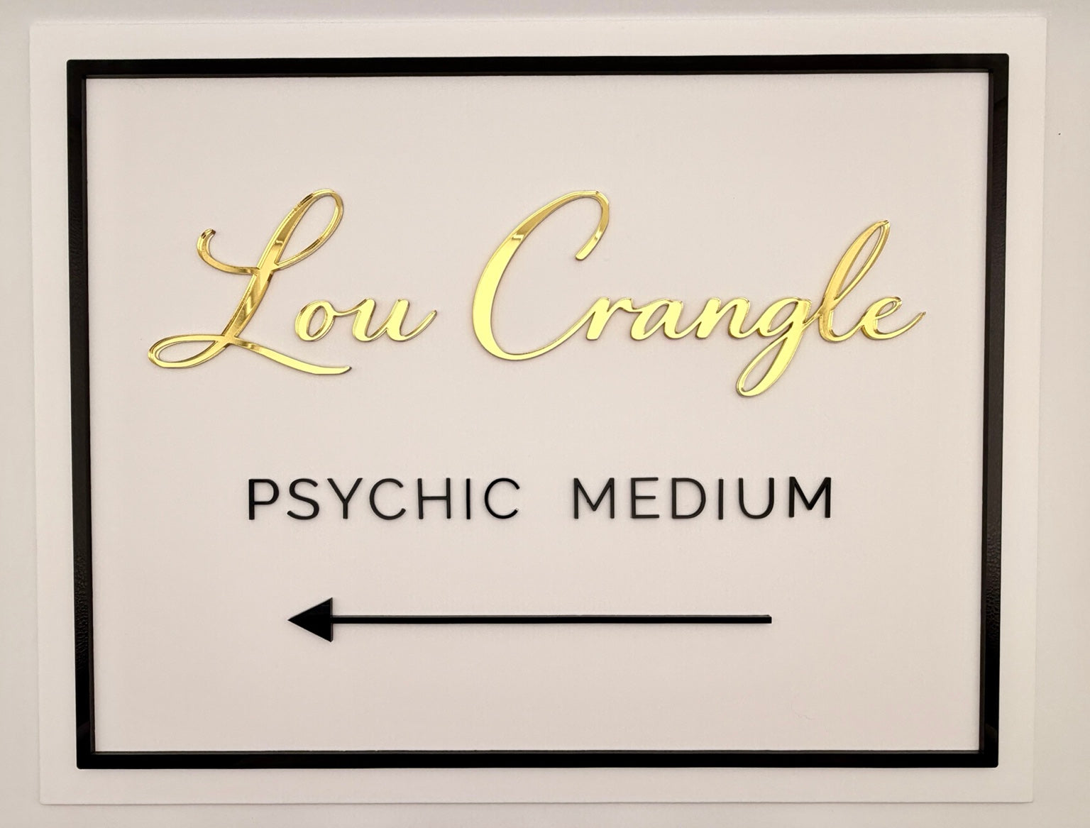Framed sign with 'Lou Crangle Psychic Medium' text in gold on a white background