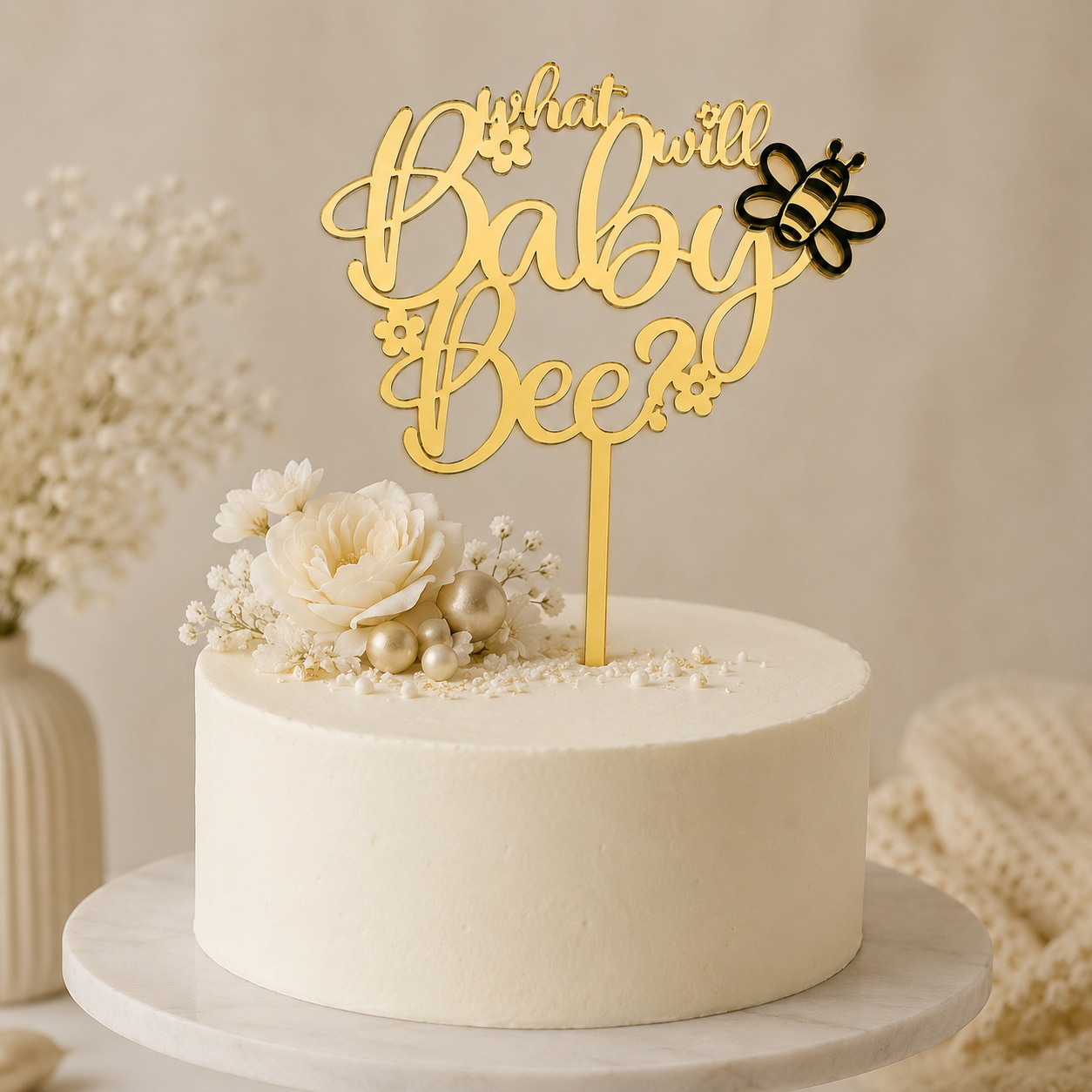 White cake with a gold 'What will baby bee?' topper on a neutral background