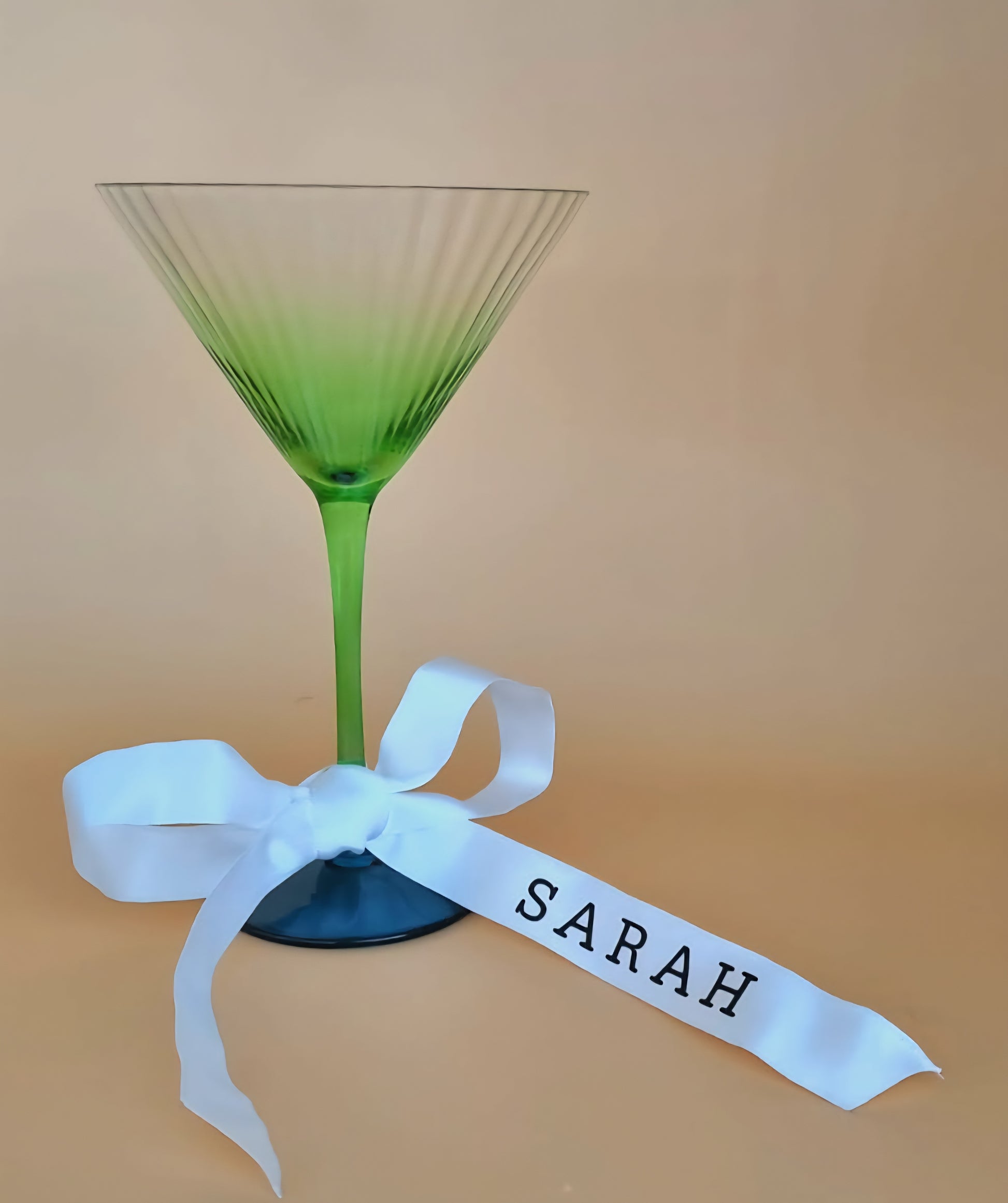 Green glass with a white ribbon labeled 'SARAH' on a beige background