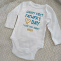 White baby onesie with 'Happy First Father's Day I Love You Daddy 2025' text on a textured surface