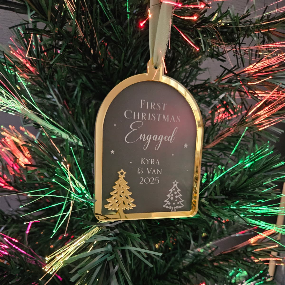 Decorative ornament tag on a Christmas tree with text 'First Christmas Engaged Kyra & Van 2025'.