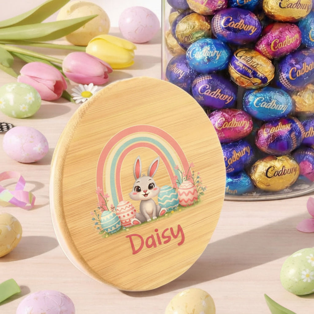 Wooden Easter egg-shaped container with a rabbit design and 'Daisy' text, surrounded by Cadbury eggs and Easter decorations.