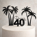 Cake topper with palm trees and 'Dave's 40th' on a white cake against a light gray background