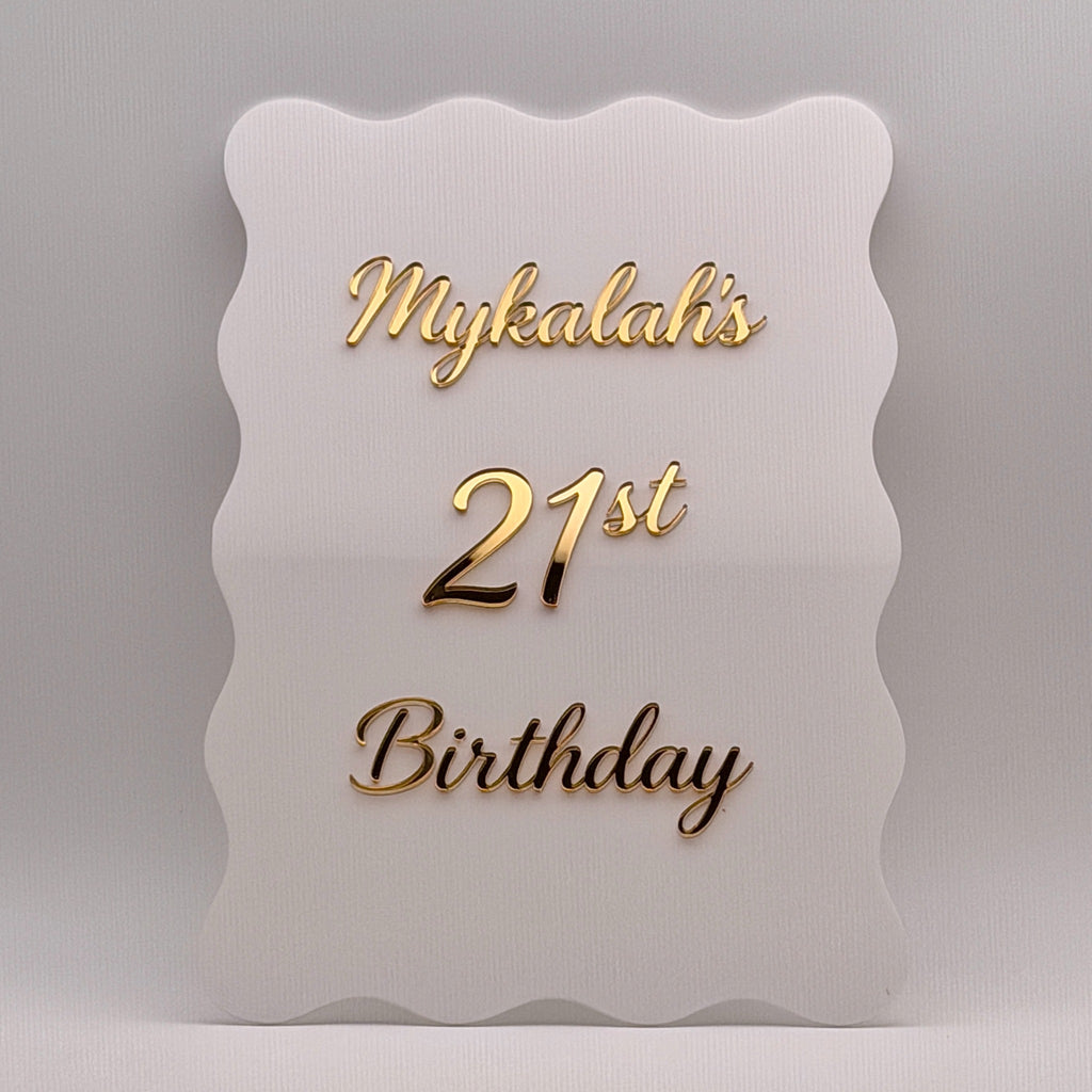 Close-up of a white wavy acrylic 21st birthday sign with raised gold mirror lettering