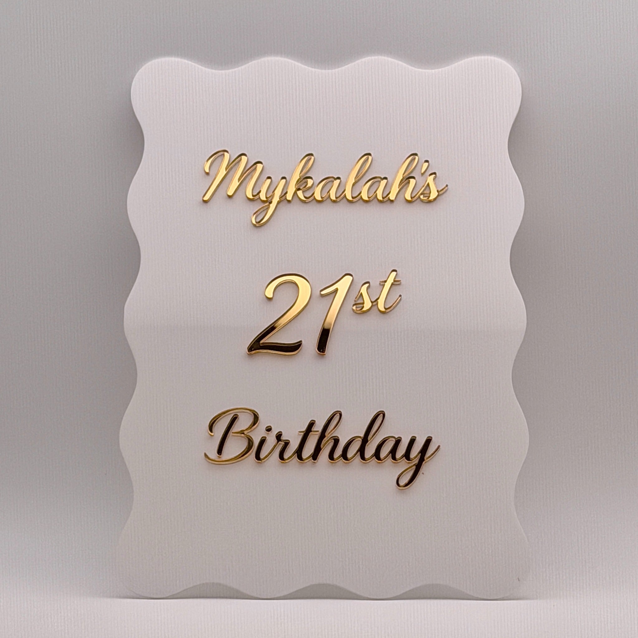 Close-up of a white wavy acrylic 21st birthday sign with raised gold mirror lettering