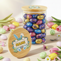 Glass jar with wooden lid filled with Cadbury eggs, decorated with Easter-themed design.
