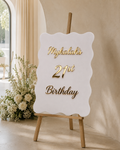 Personalised A1 white wavy acrylic 21st birthday event sign with raised gold lettering on an easel
