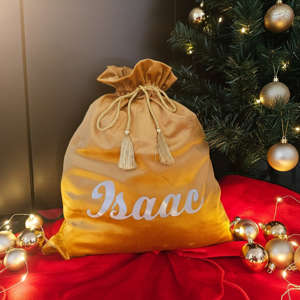 Gold drawstring bag with 'Isaac' printed on it, placed against a red fabric background.