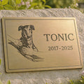 Brass plaque with a dog illustration and engraved name and years on a stone surface.