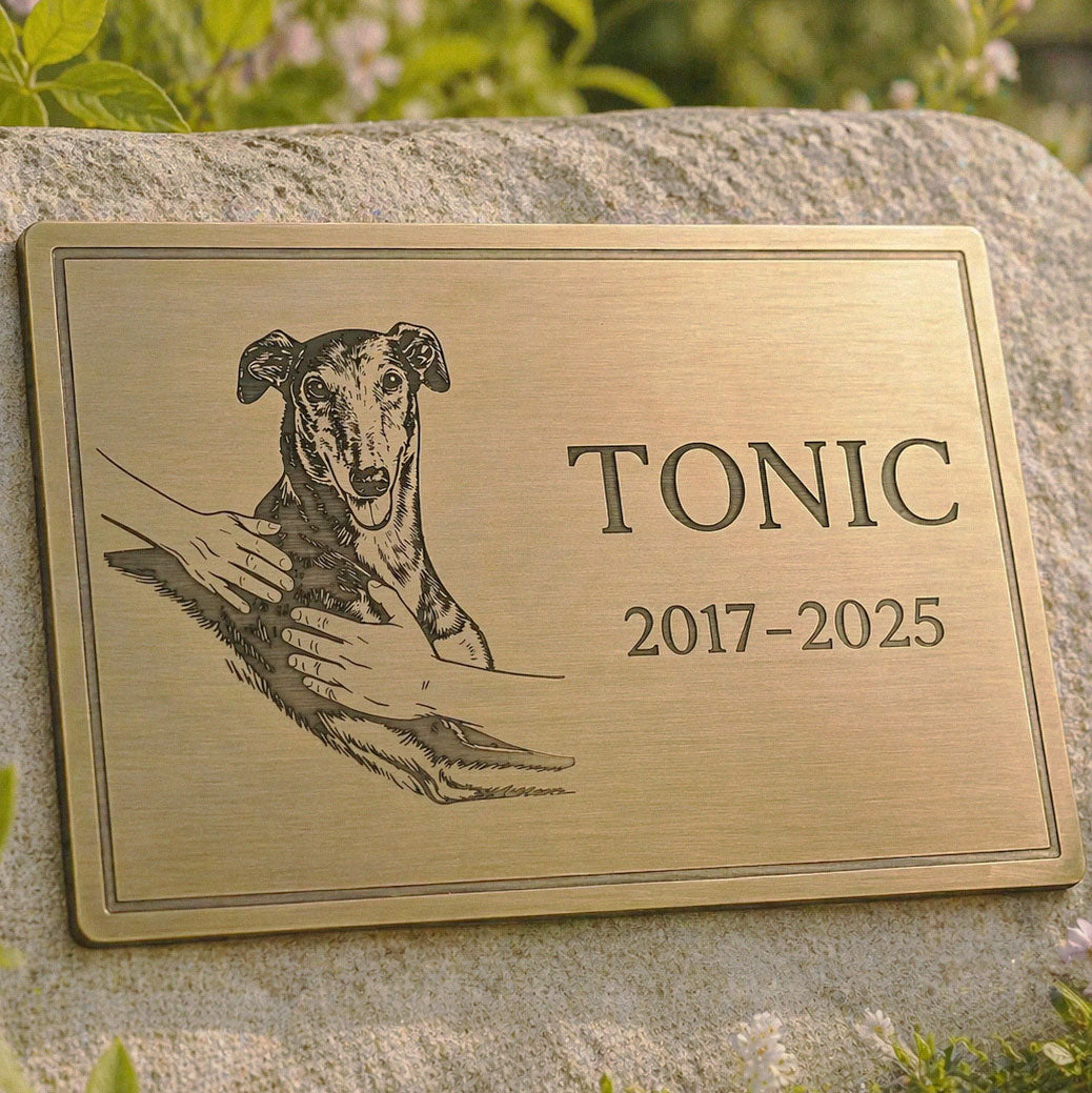 Brass plaque with a dog illustration and engraved name and years on a stone surface.
